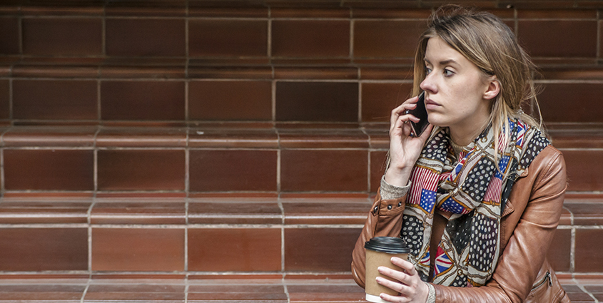 Woman on phone with coffee on staircase
