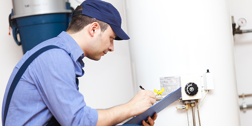 Contractor with blue shirt and hat taking notes and working on a hot water tank